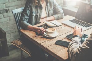 Teamwork. Businessman and businesswoman sitting at table in coffee shop and discuss business plan. On table is laptop, tablet, smartphone, notebook, cup of coffee.Business meeting of partners in cafe.